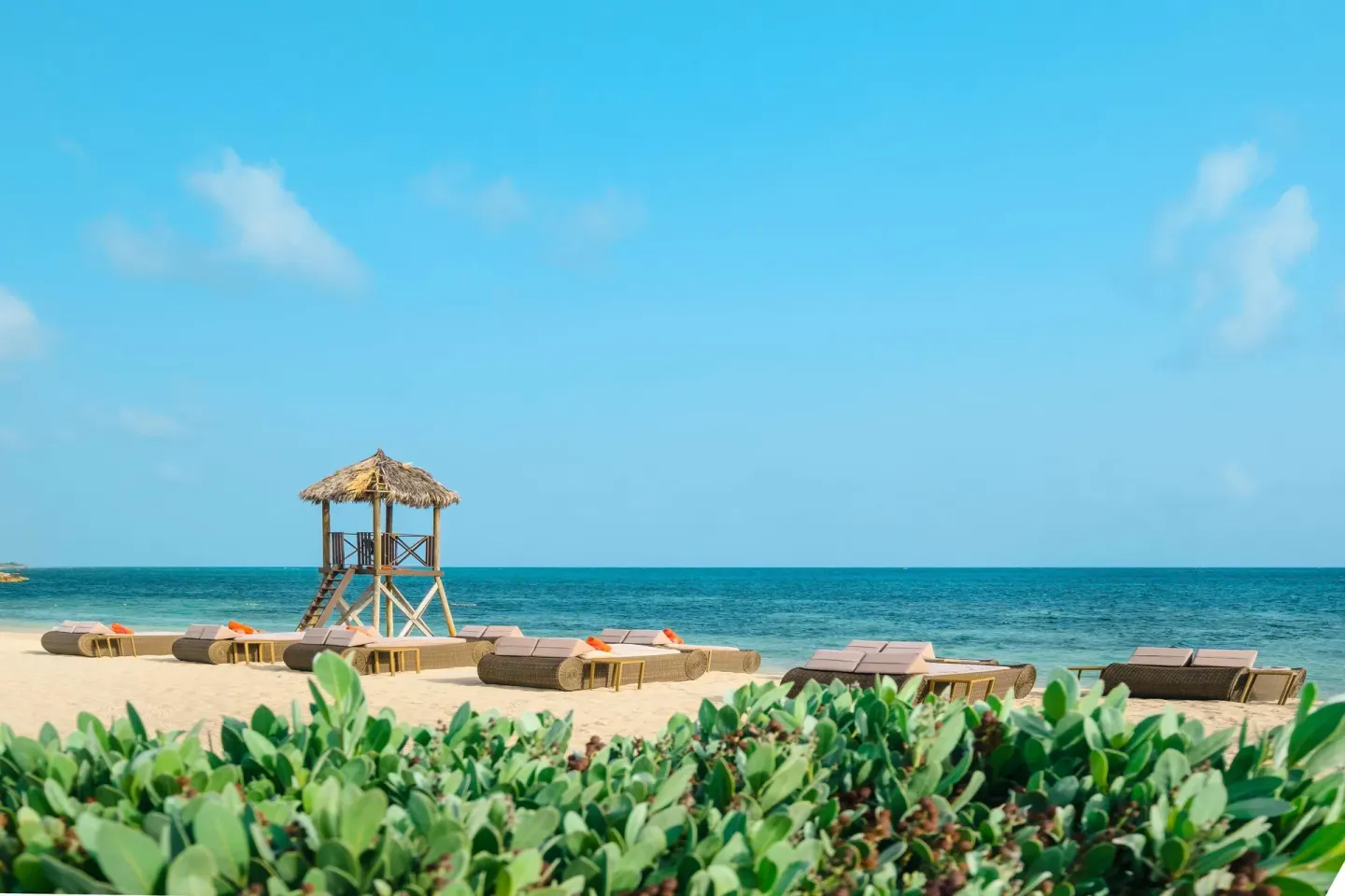 Oceanfront beach loungers and thatched lifeguard stand at JOIA Rose Hall by Iberostar.