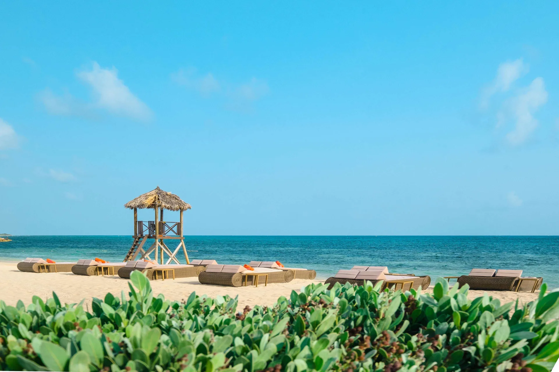 Oceanfront beach loungers and thatched lifeguard stand at JOIA Rose Hall by Iberostar.