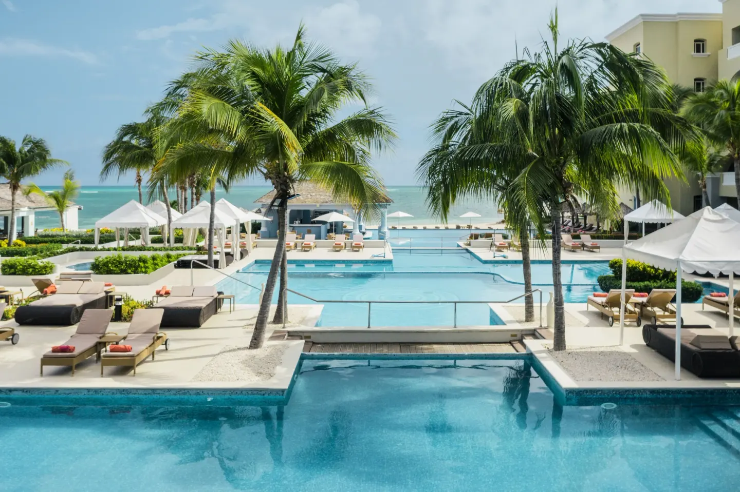 Oceanfront pool with palms, loungers, and cabanas at JOIA Rose Hall by Iberostar.