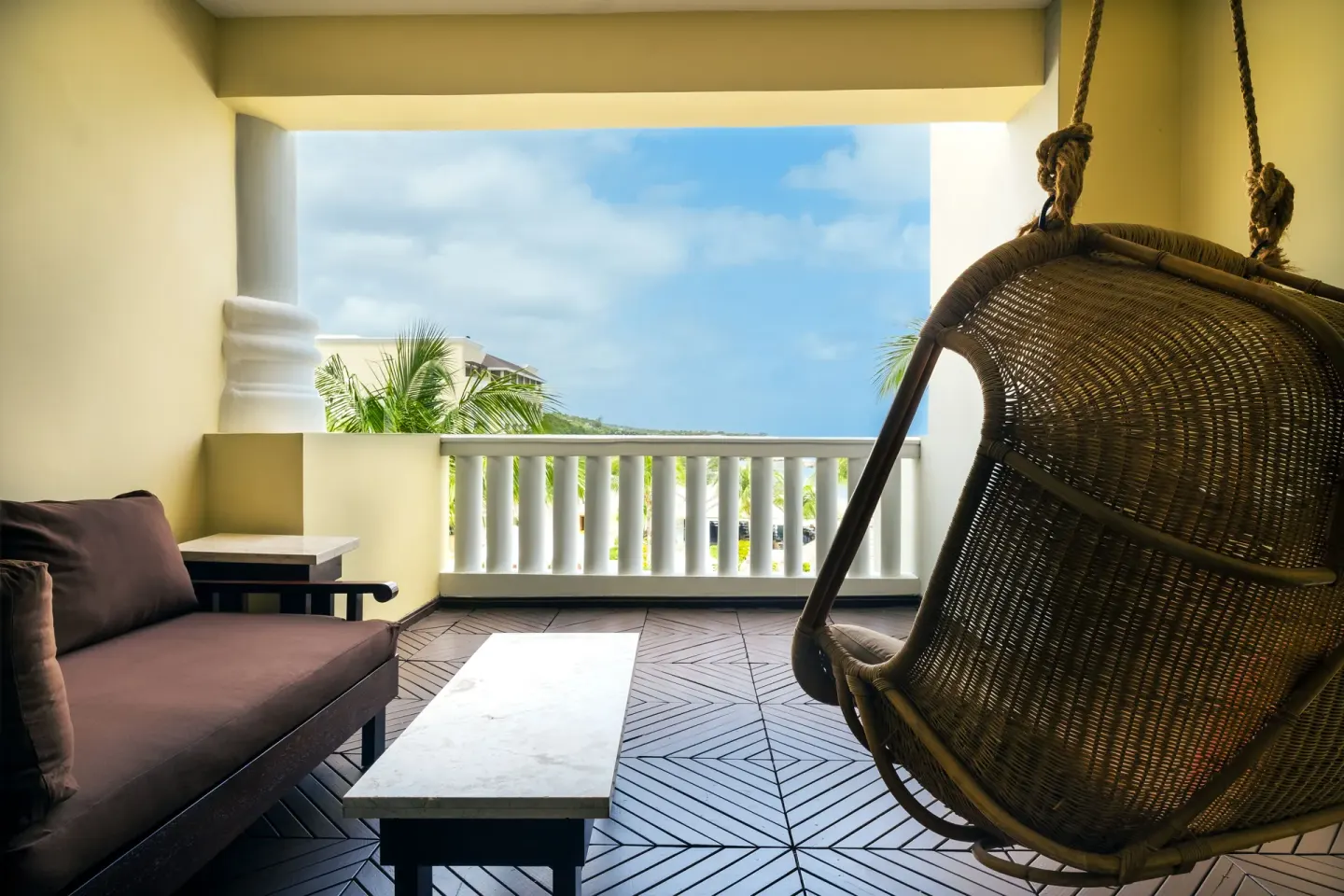 Covered balcony with hanging chair, sofa and partial ocean view at JOIA Rose Hall by Iberostar.