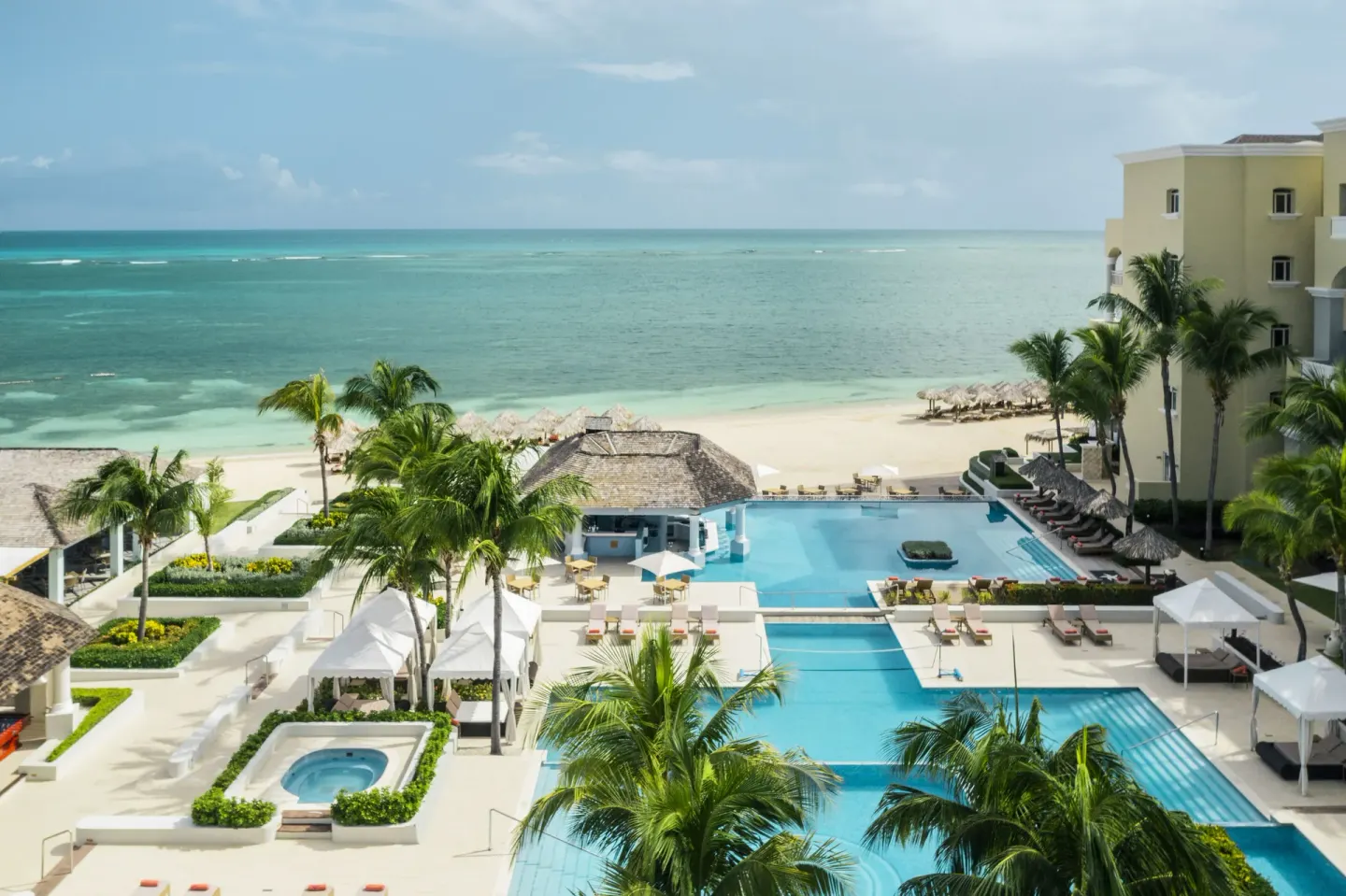 Pool complex with palm trees and ocean backdrop at JOIA Rose Hall by Iberostar.