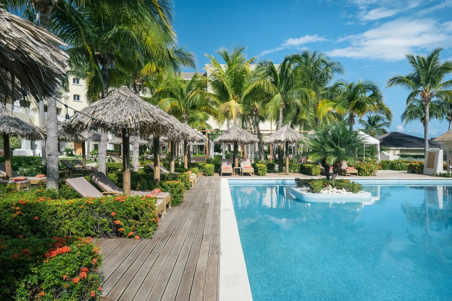 Pool deck with palapas, loungers, and tropical flowers at JOIA Rose Hall by Iberostar.