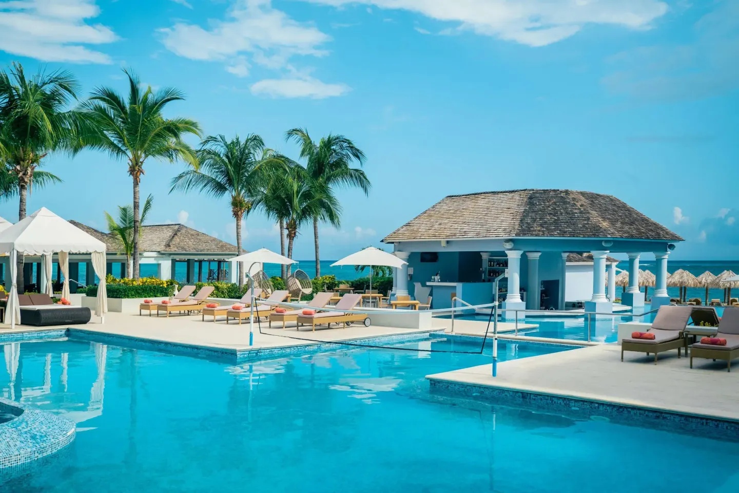 Pool deck with swim-up bar and ocean beyond at JOIA Rose Hall by Iberostar.