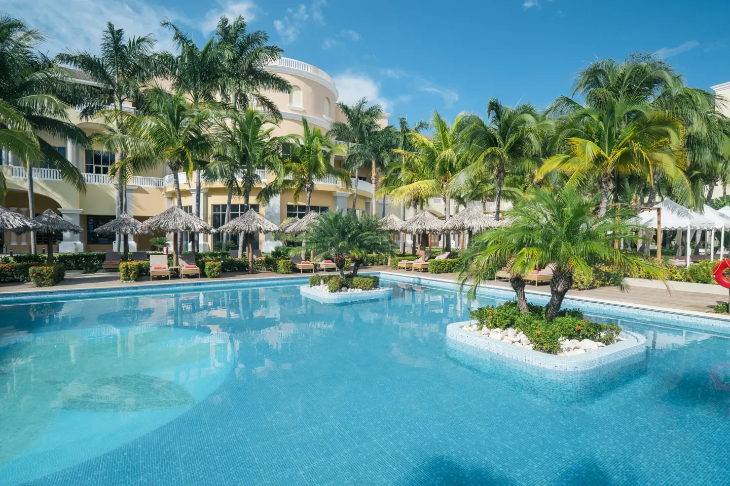 Pool with island planters, palms, and palapas at JOIA Rose Hall by Iberostar.