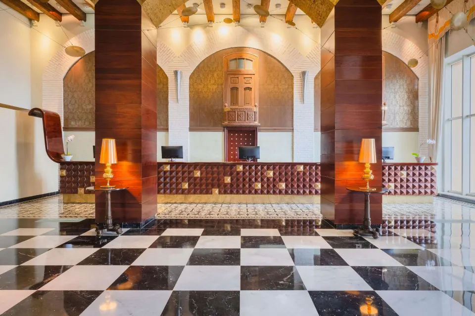 Reception area at JOIA Rose Hall by Iberostar with check-in desks, wood columns, and checkerboard floor.