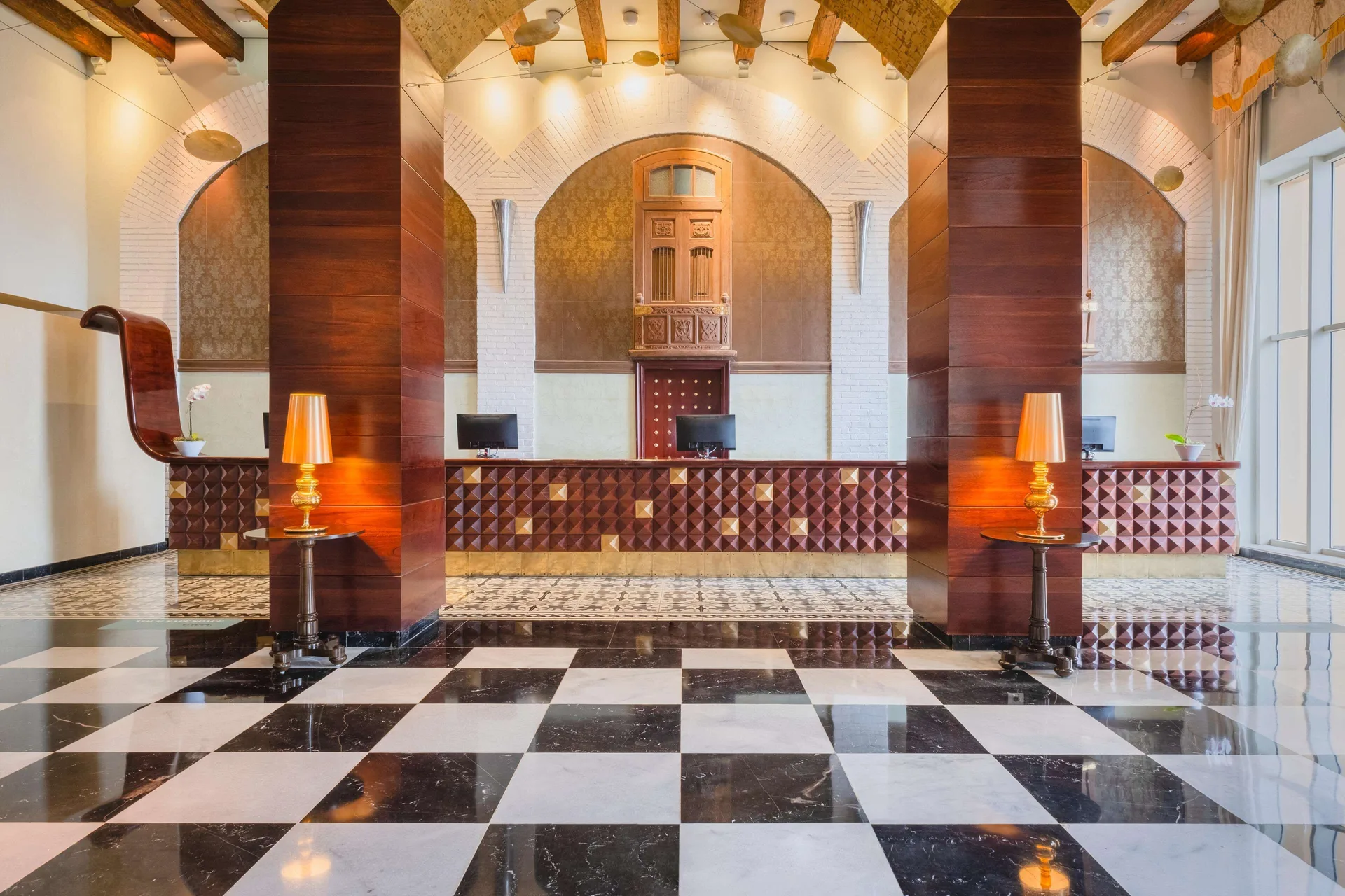 Reception area at JOIA Rose Hall by Iberostar with check-in desks, wood columns, and checkerboard floor.