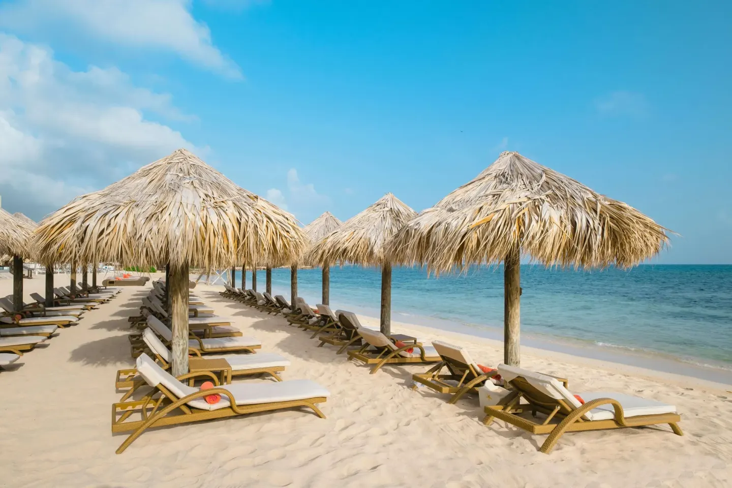 Thatched beach umbrellas and loungers beside the sea at JOIA Rose Hall by Iberostar.