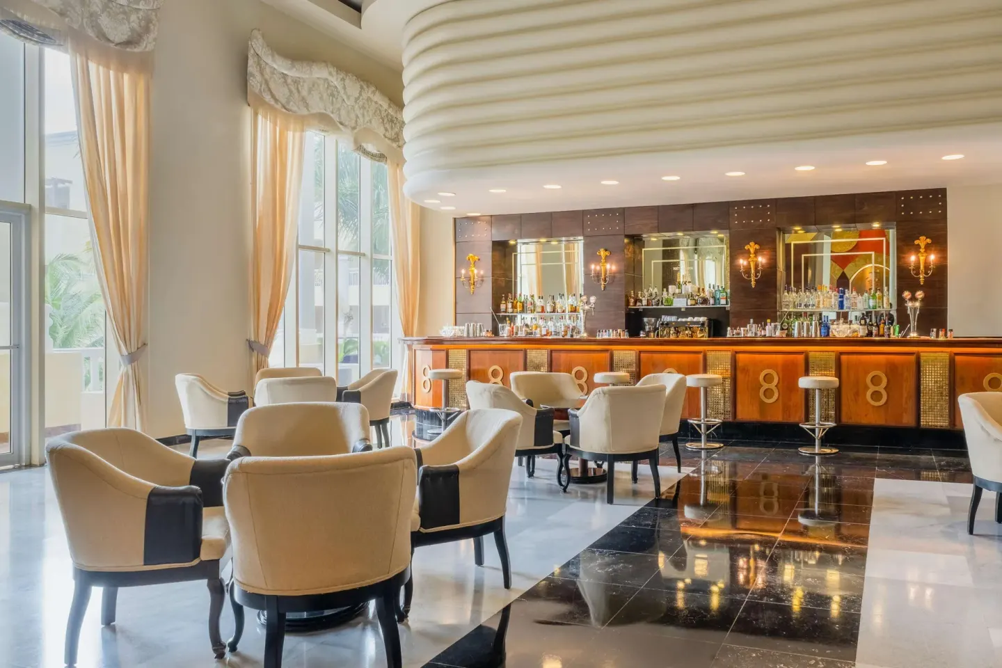 Elegant lobby bar with cream seating and tall windows at JOIA Rose Hall by Iberostar.