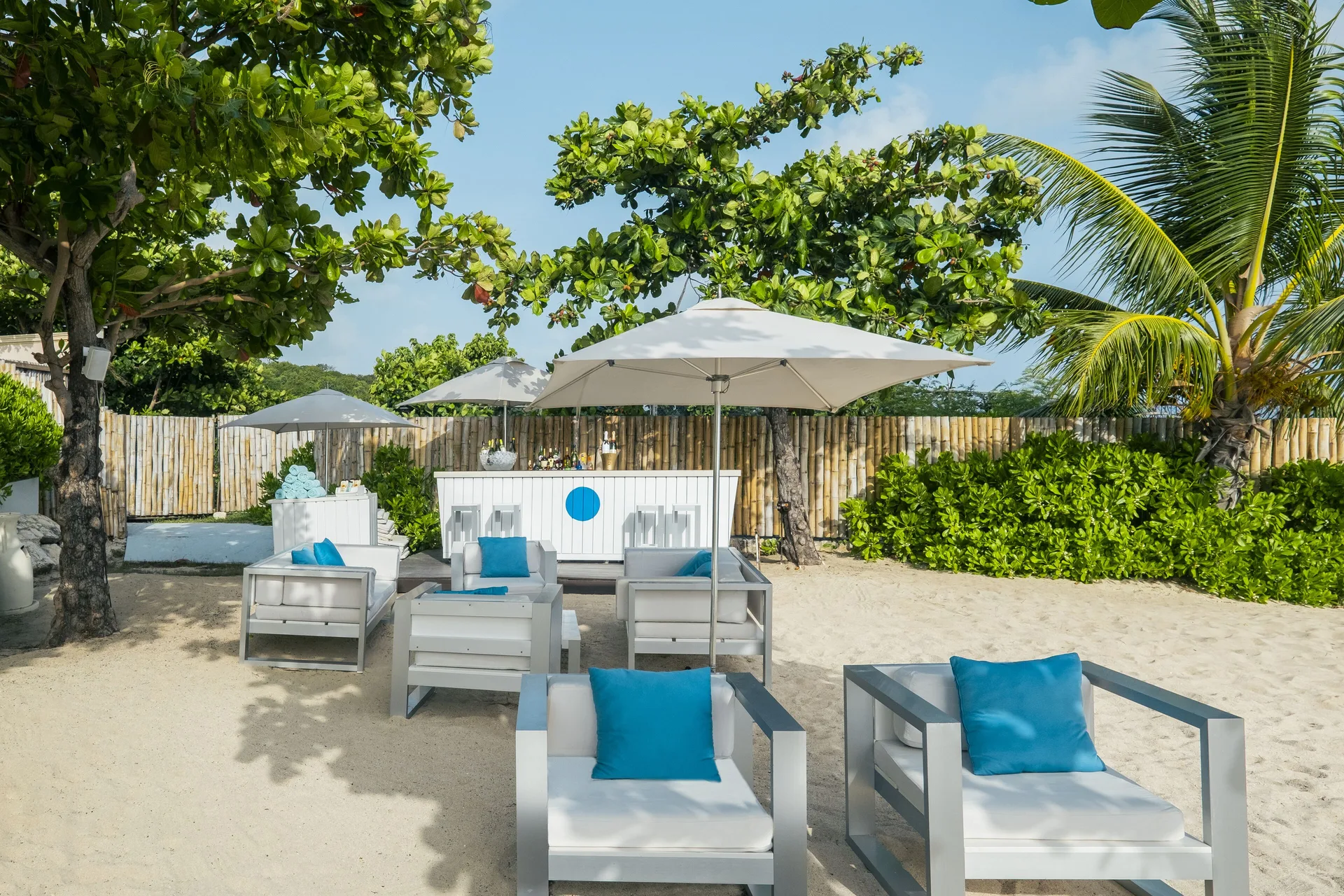 Beach lounge seating and bar under trees at JOIA Rose Hall by Iberostar.