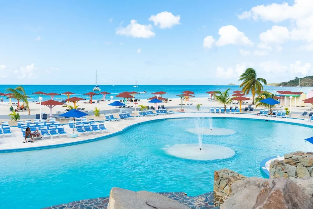 Beachfront pool with fountains, loungers, umbrellas, and sea views at Jolly Beach Antigua.