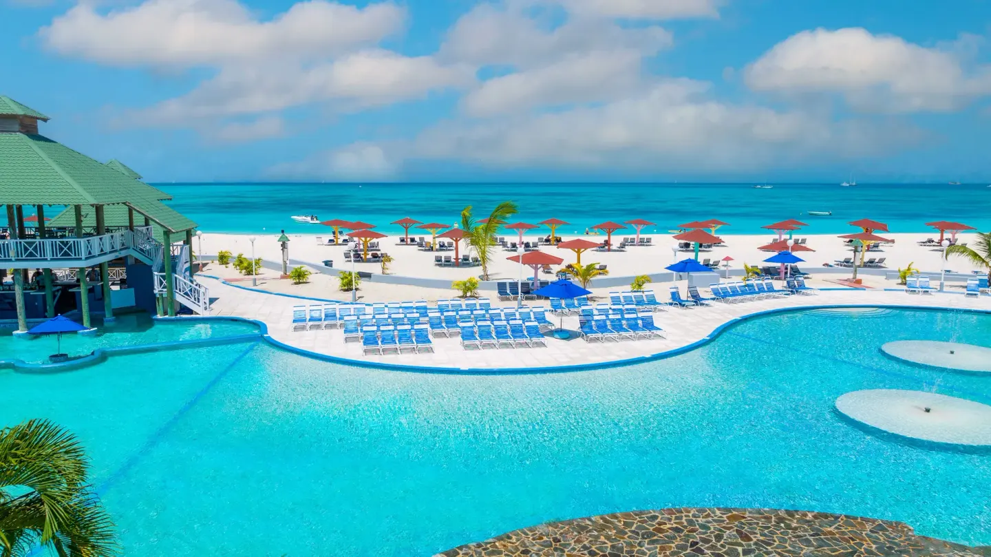 Beachfront pool with loungers, umbrellas and the sea beyond at Jolly Beach Antigua.