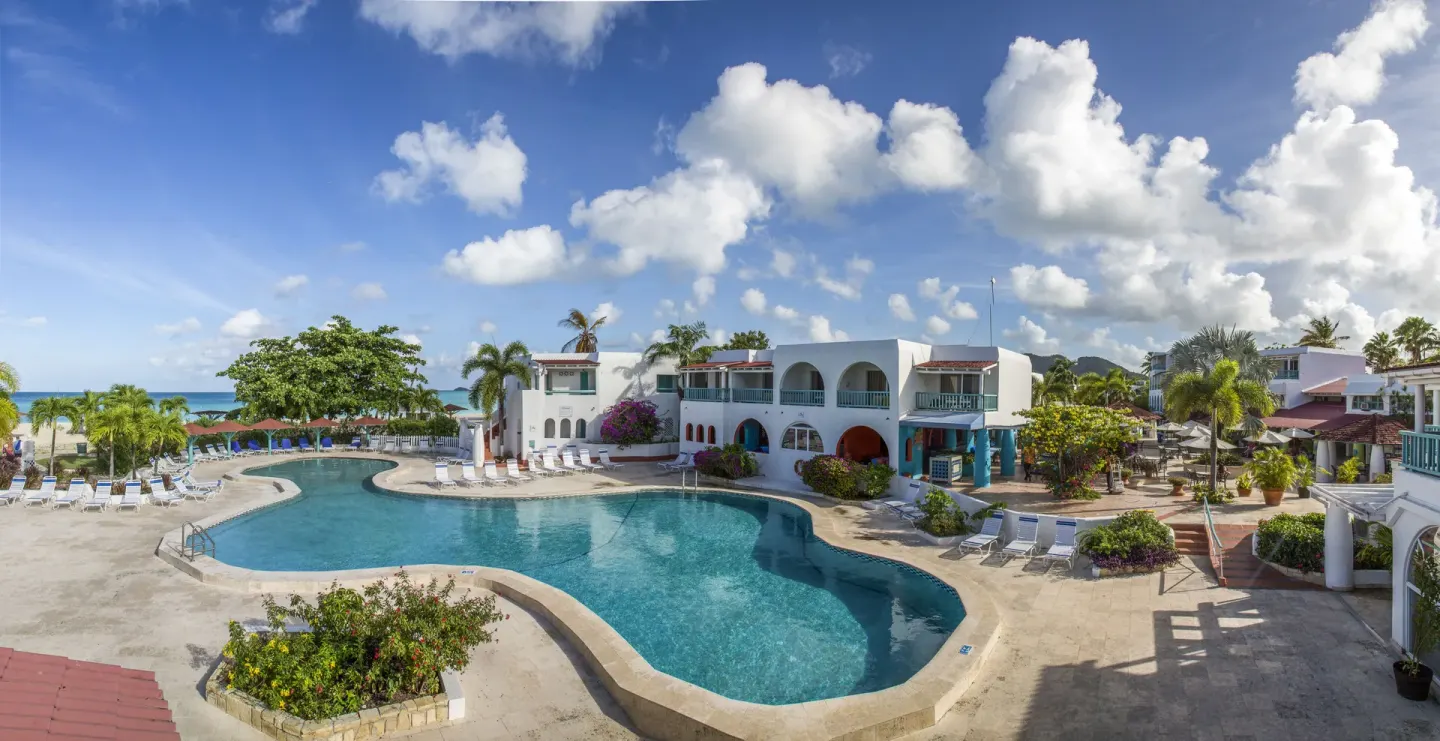 Curved swimming pool beside white resort buildings at Jolly Beach Antigua.