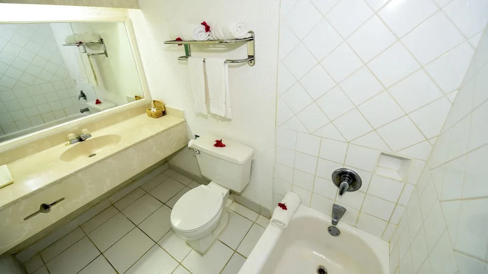 Guest bathroom with tub, toilet, long vanity and towel shelf at Jolly Beach Antigua.