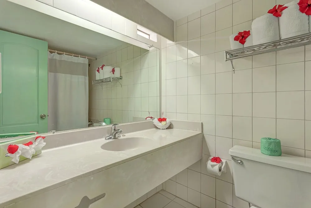 Guest bathroom vanity with mirror, toilet, towels and flower accents at Jolly Beach Antigua.
