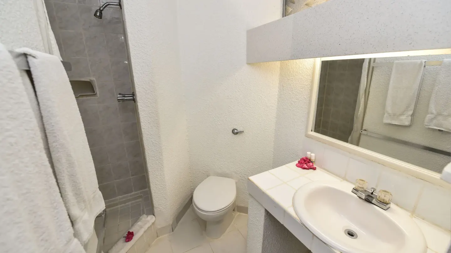 Compact bathroom with shower, toilet, sink, mirror and towels at Jolly Beach Antigua.