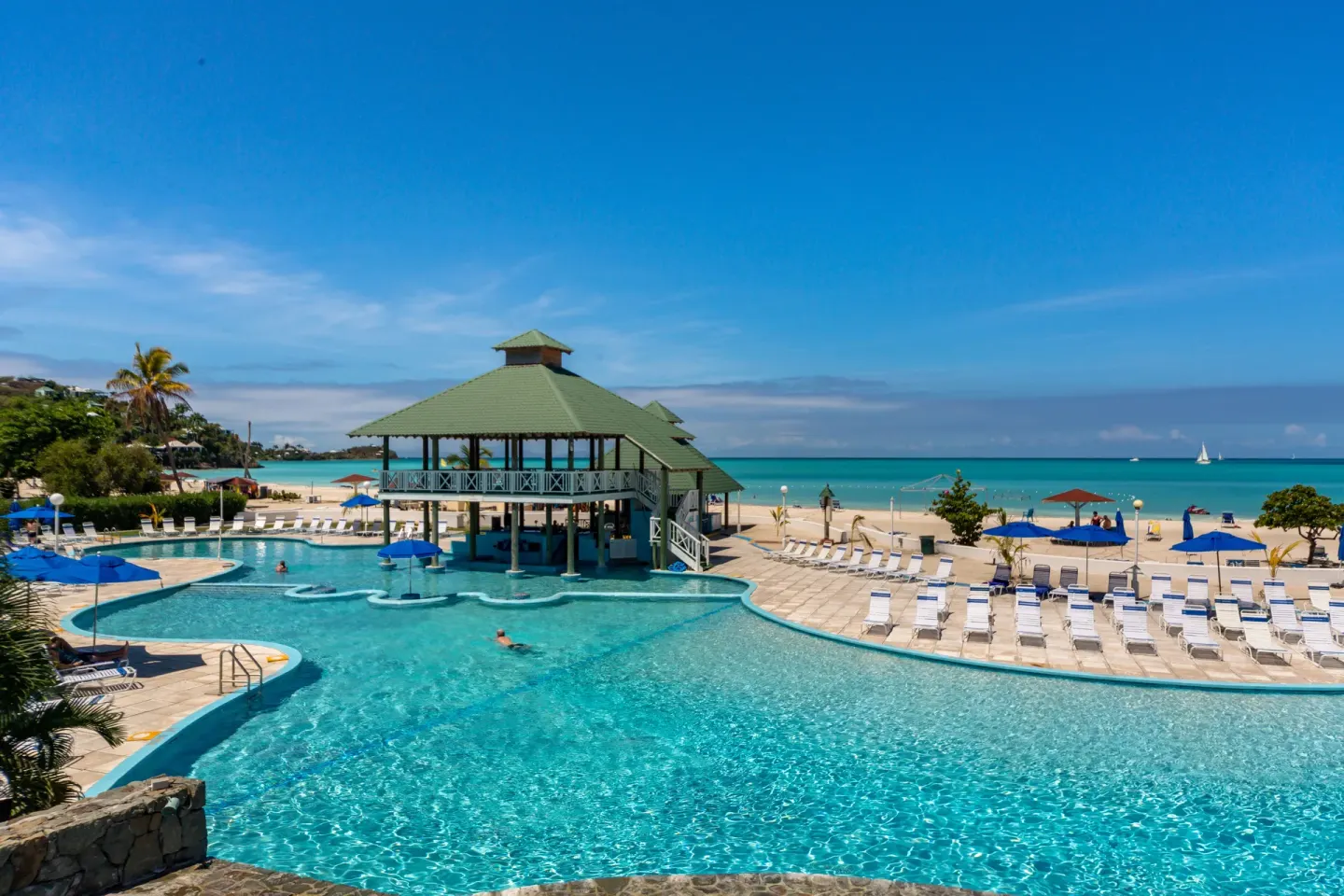 Main pool, swim-up pavilion, and beach at Jolly Beach Antigua under a clear blue sky.