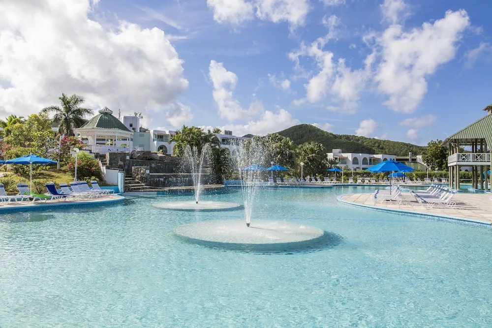 Large resort pool with fountain jets, loungers and hillside backdrop at Jolly Beach Antigua.