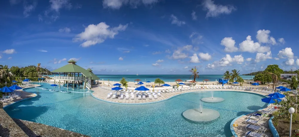 Panoramic view of pools, loungers, beach, and sea at Jolly Beach Antigua.