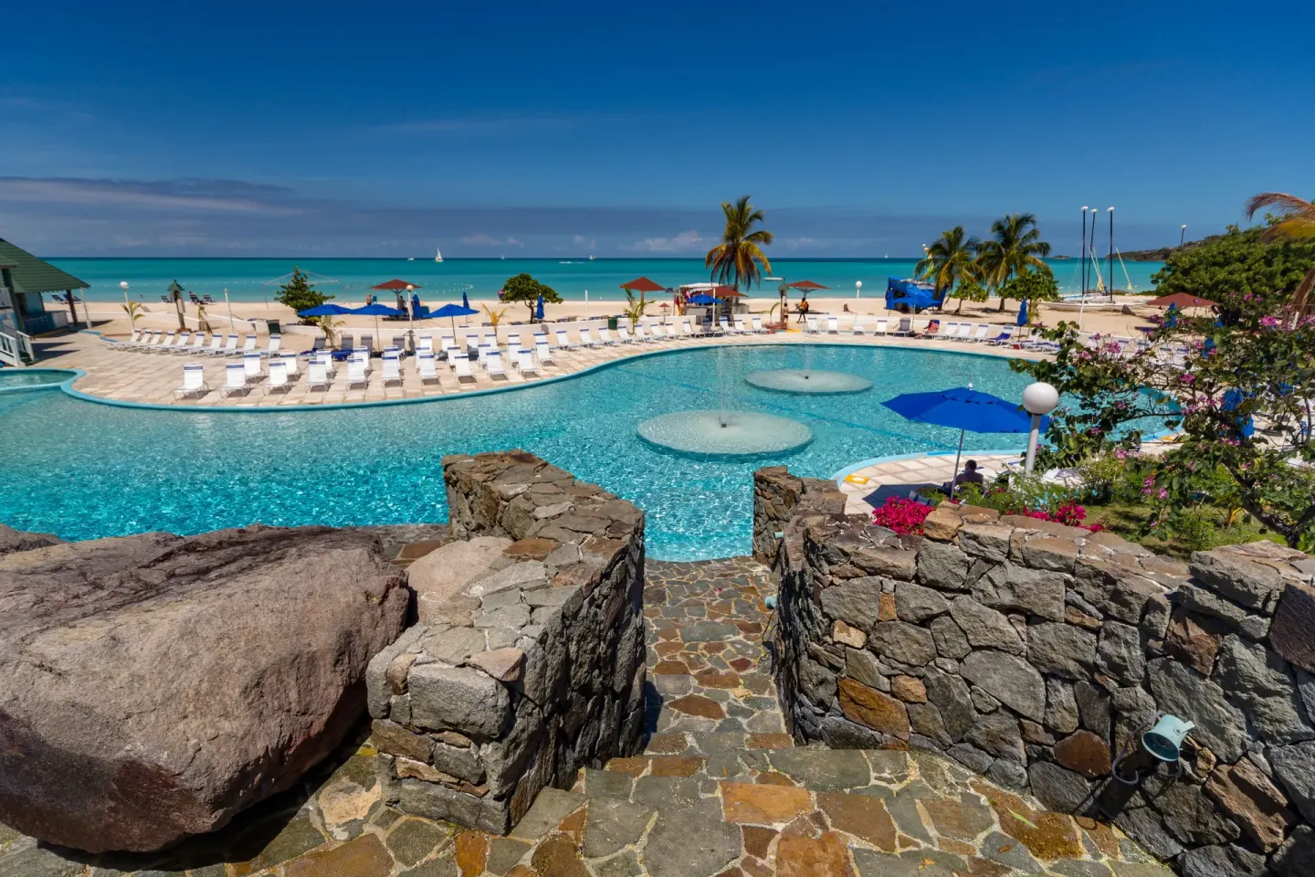 Elevated view of the pool, stone steps, beach and turquoise sea at Jolly Beach Antigua.