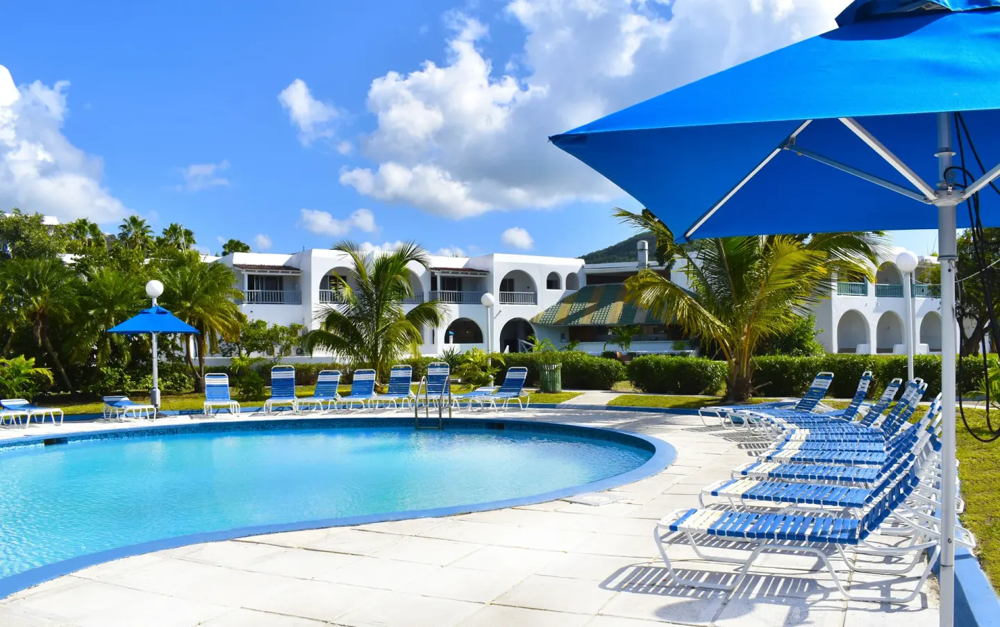 Quiet pool deck with blue loungers and white guest buildings at Jolly Beach Antigua.