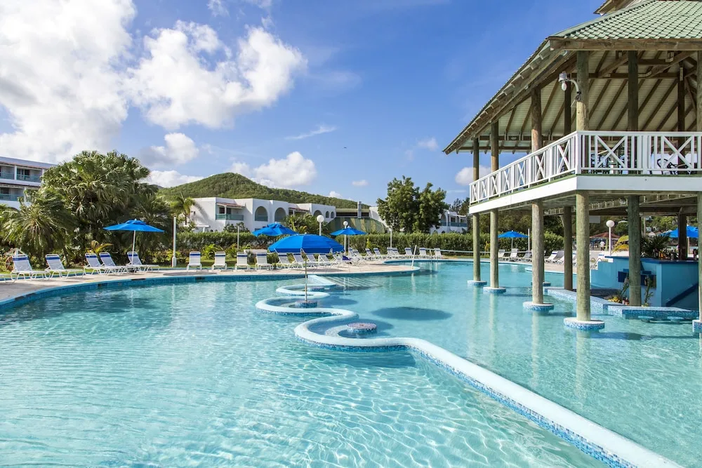 Pool with shaded loungers, pavilion posts, and resort buildings at Jolly Beach Antigua.