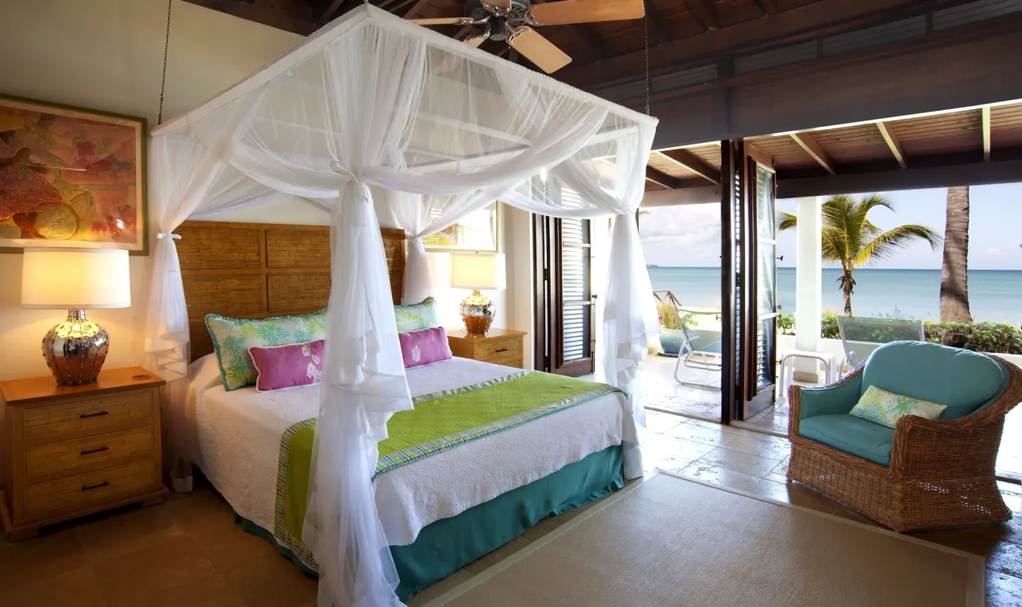 Canopy king bed opens to a beachfront patio at Jumby Bay Island.