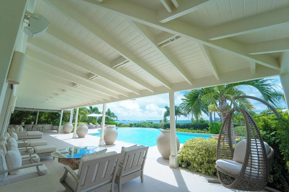 Covered poolside veranda at Jumby Bay Island with white seating, a hanging chair, and ocean views.