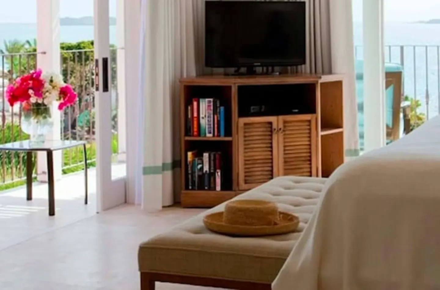 Guest room sitting area with TV, bed edge and balcony sea view at Jumby Bay Island.