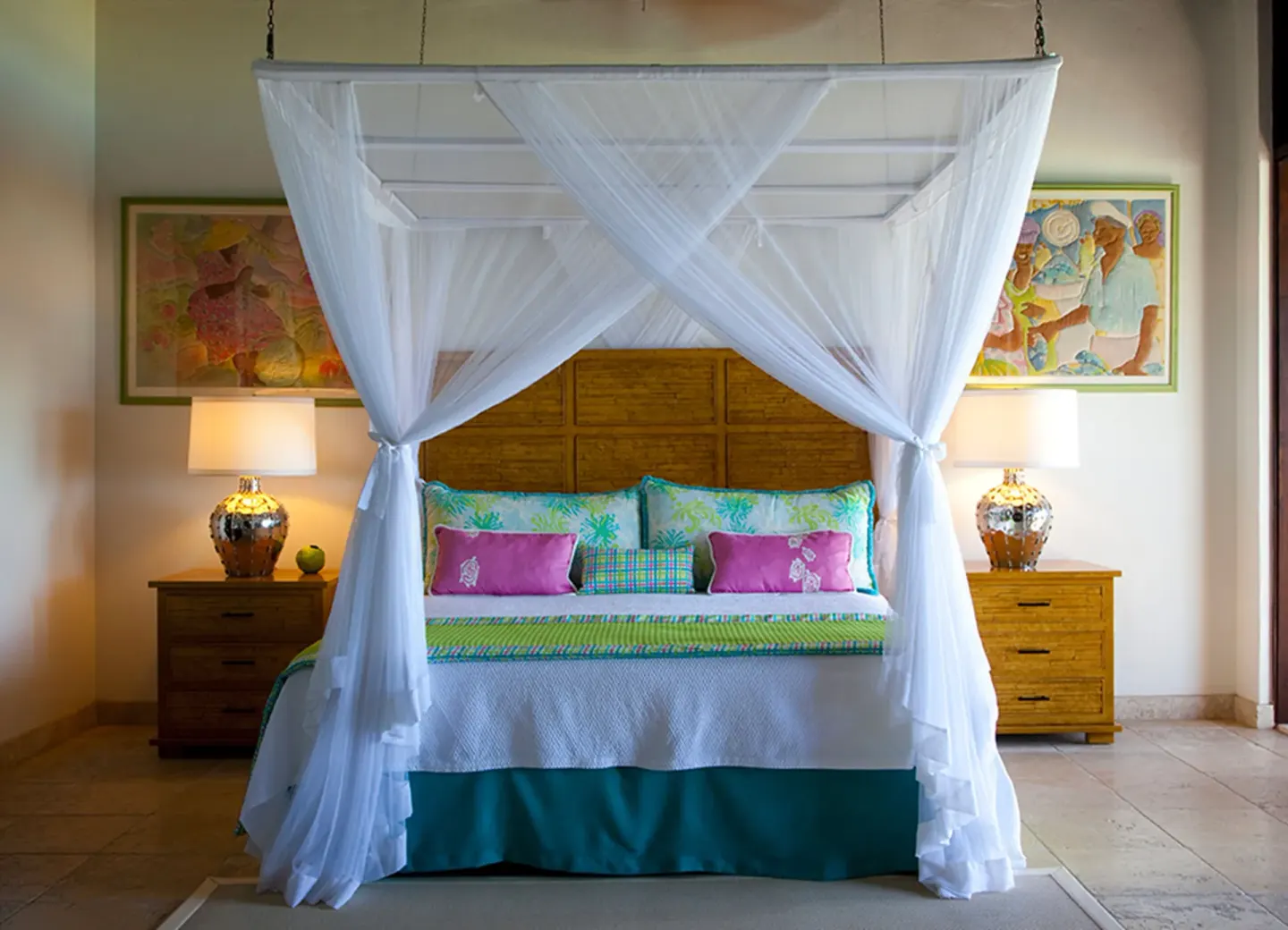 Canopy bed with white netting and colorful pillows in a guest room at Jumby Bay Island.