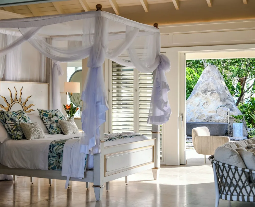 Guest room with a four-poster canopy bed and open doors to an outdoor tub at Jumby Bay Island.