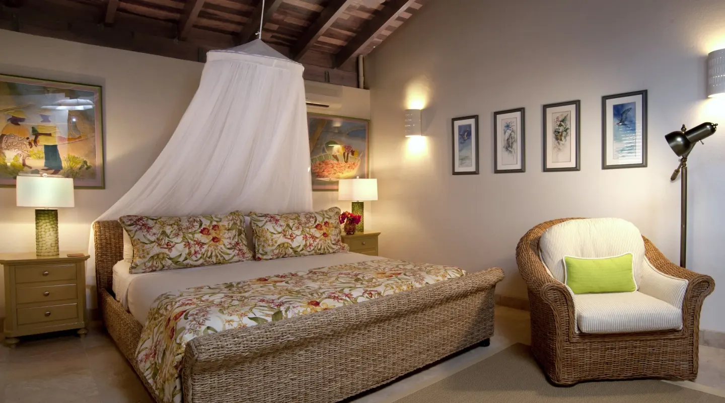 Wicker king bed with floral bedding and canopy netting at Jumby Bay Island.