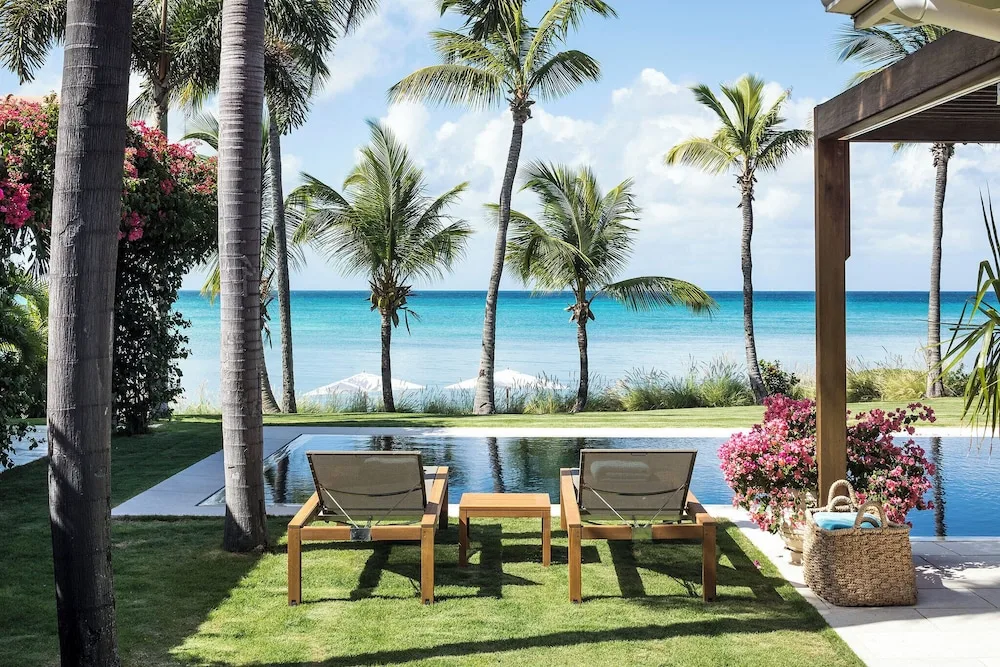 Oceanfront pool lawn with two loungers, palms and sea views at Jumby Bay Island.