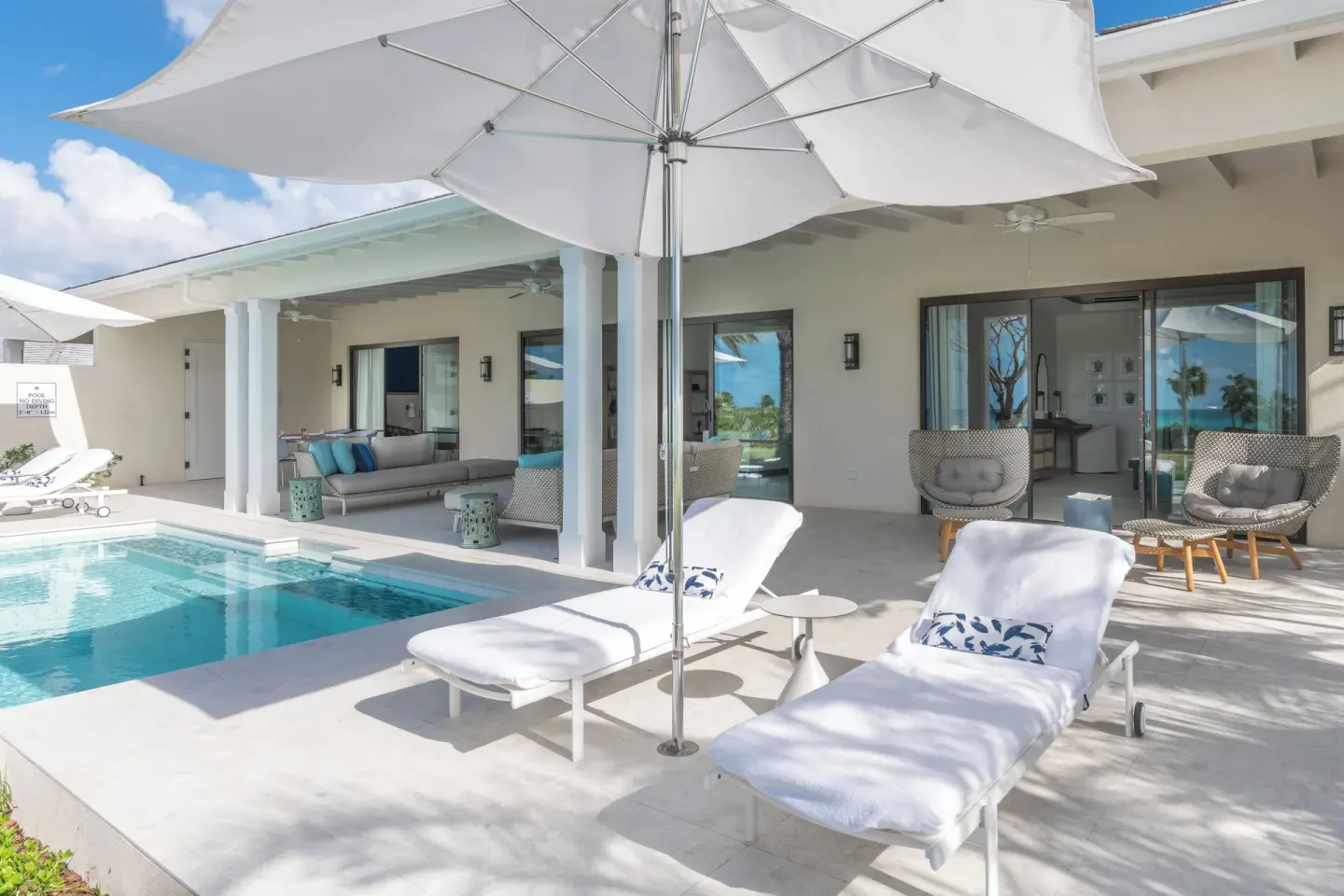 Pool terrace with white loungers, umbrellas and covered seating at Jumby Bay Island.
