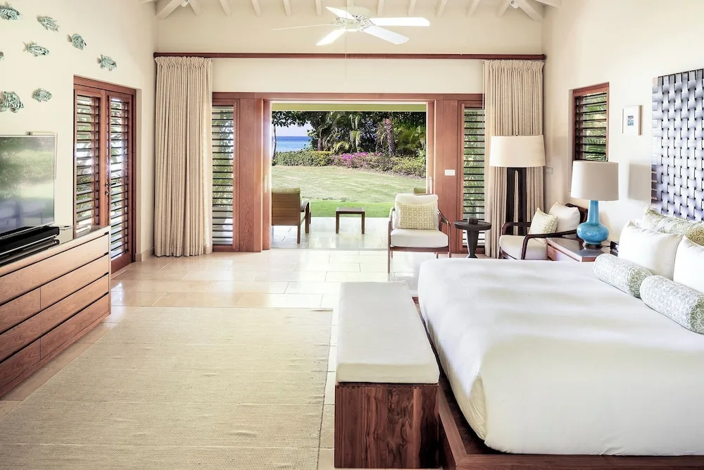 Guest room with king bed and open doors to a lawn and sea view at Jumby Bay Island.