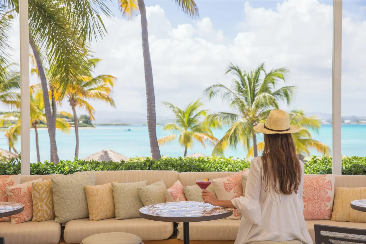 Guest holding a cocktail on a cushioned terrace with ocean views at Jumby Bay Island.