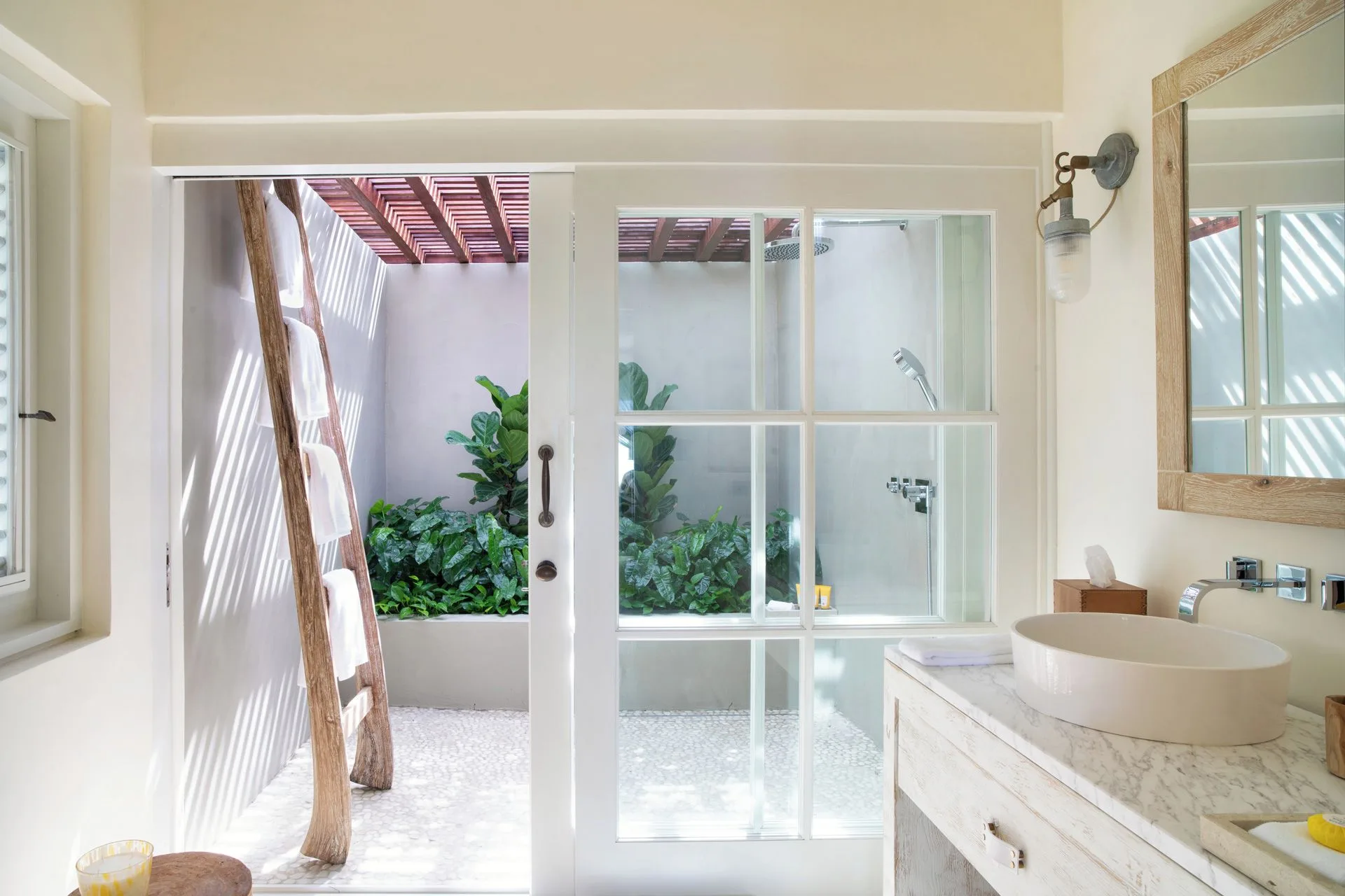 Calabash bathroom at Jumby Bay Island with a vessel sink and glass doors to an outdoor shower.