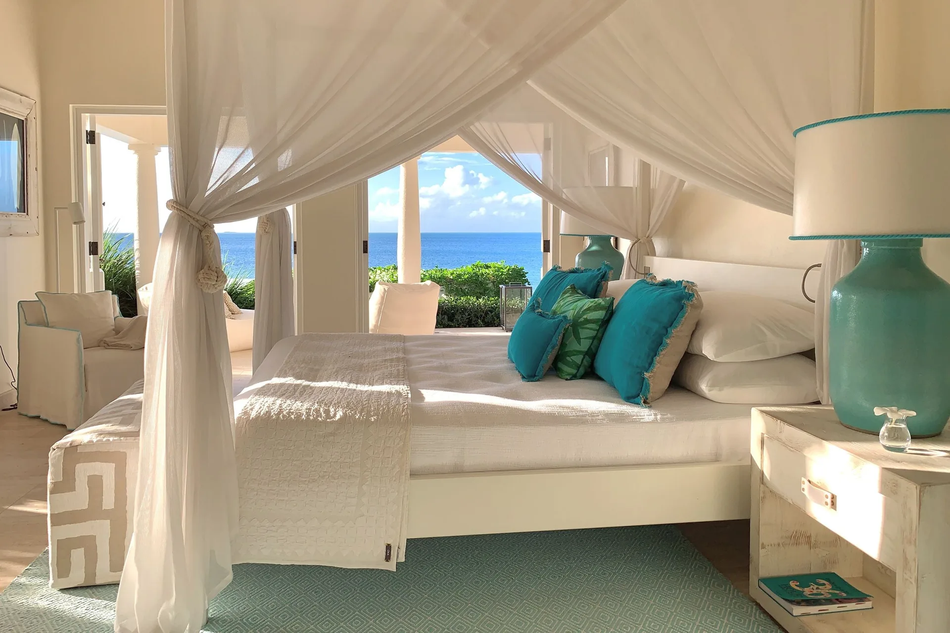 Calabash guest room at Jumby Bay Island with a canopied bed and ocean view through open doors.