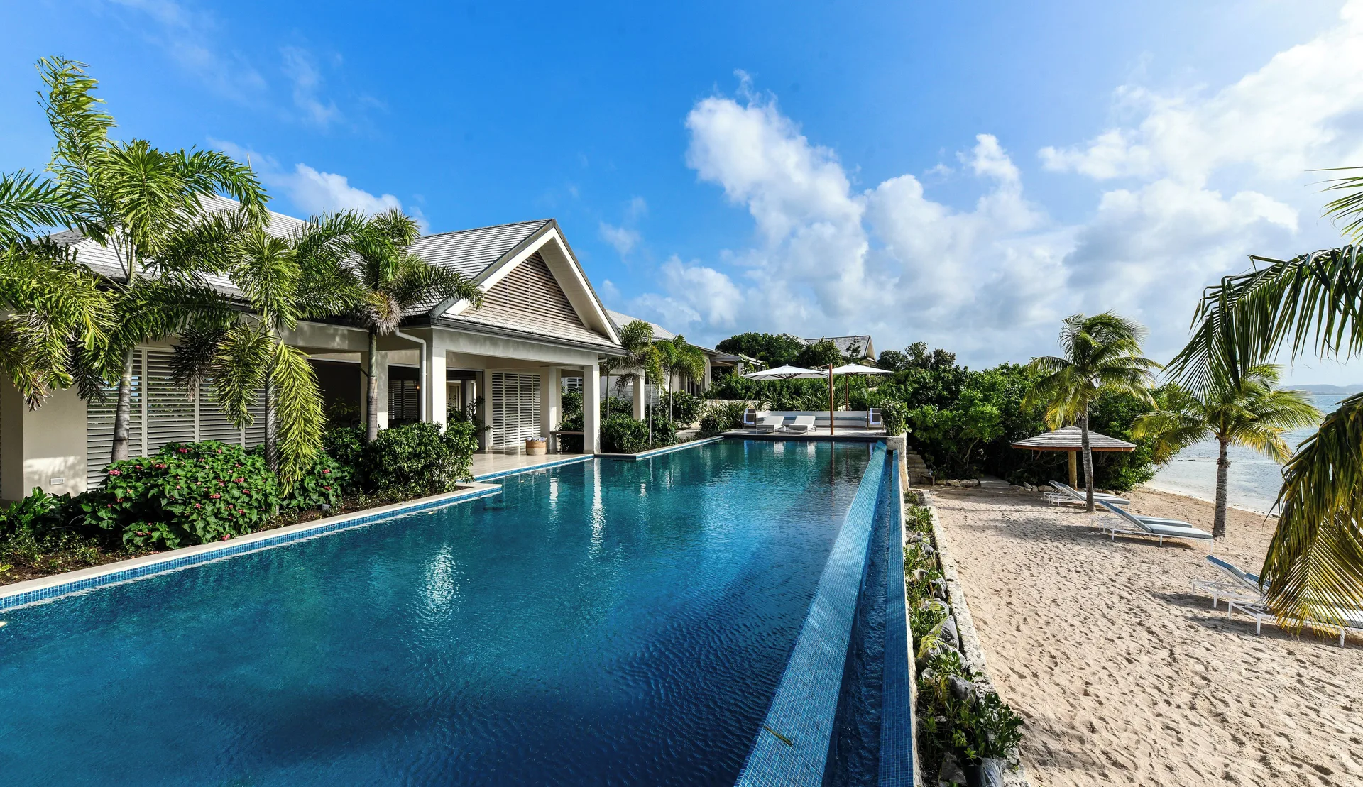 Delphis exterior with long pool and beach beside the villa at Jumby Bay Island.