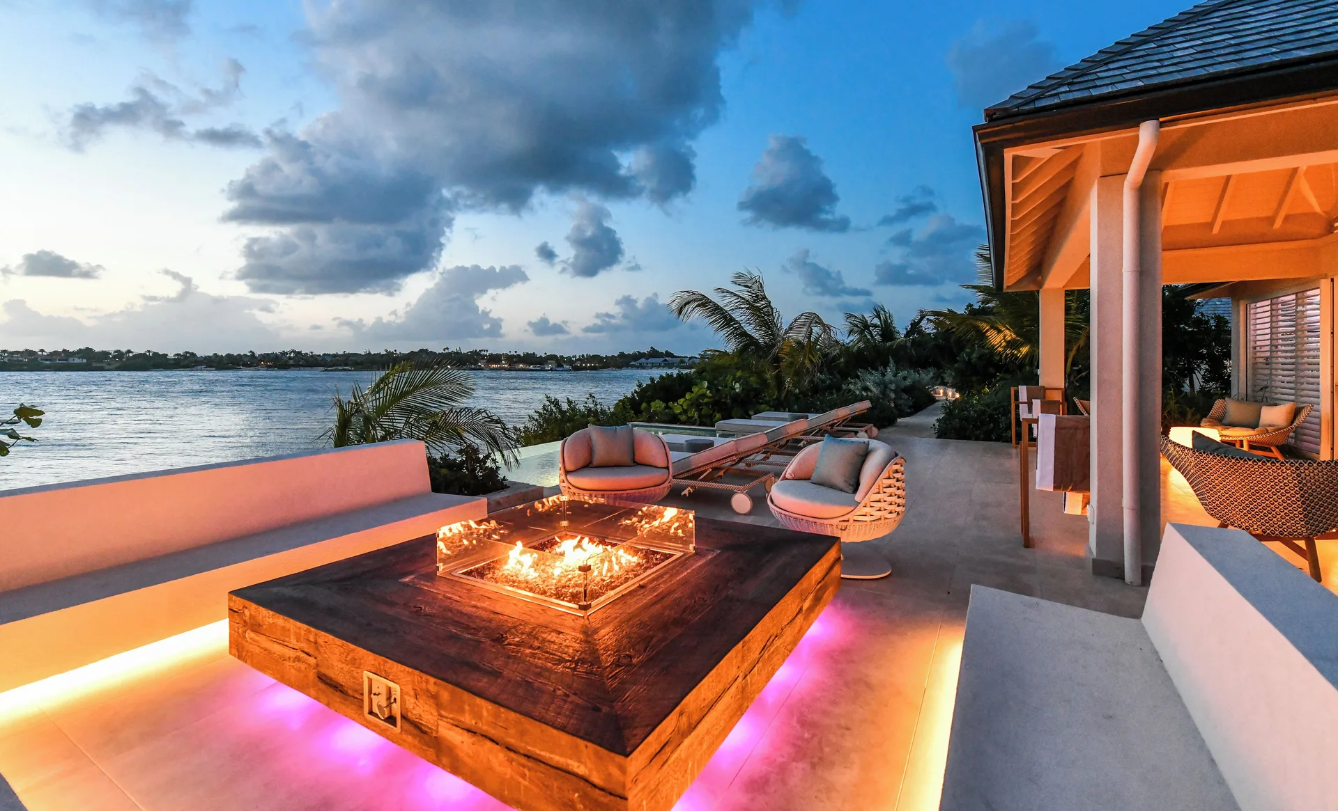 Delphis waterfront terrace with fire feature at dusk at Jumby Bay Island.
