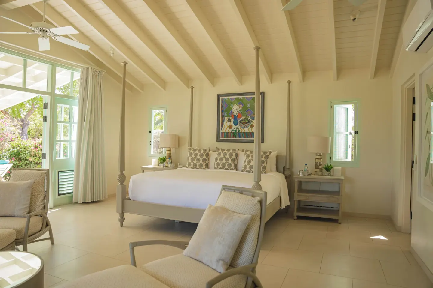 Dragonfly guest room at Jumby Bay Island with four-poster bed, lounge chair, and garden-facing doors.