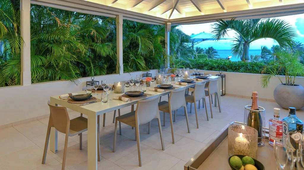 Dragonfly terrace at Jumby Bay Island set for dining beside palms and a blue ocean view.