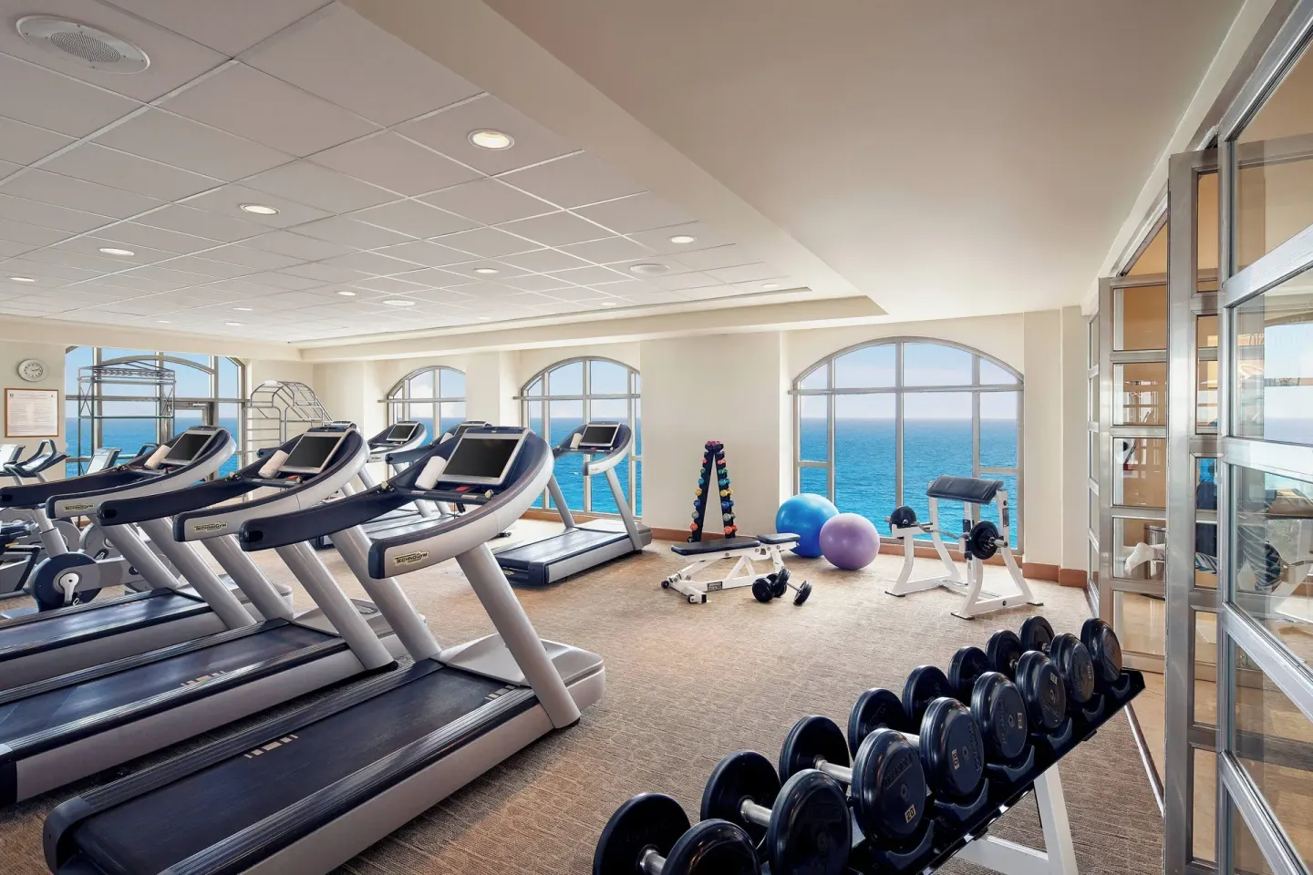 Fitness center with treadmills, weights, and arched ocean-view windows at JW Marriott Cancun Resort & Spa.