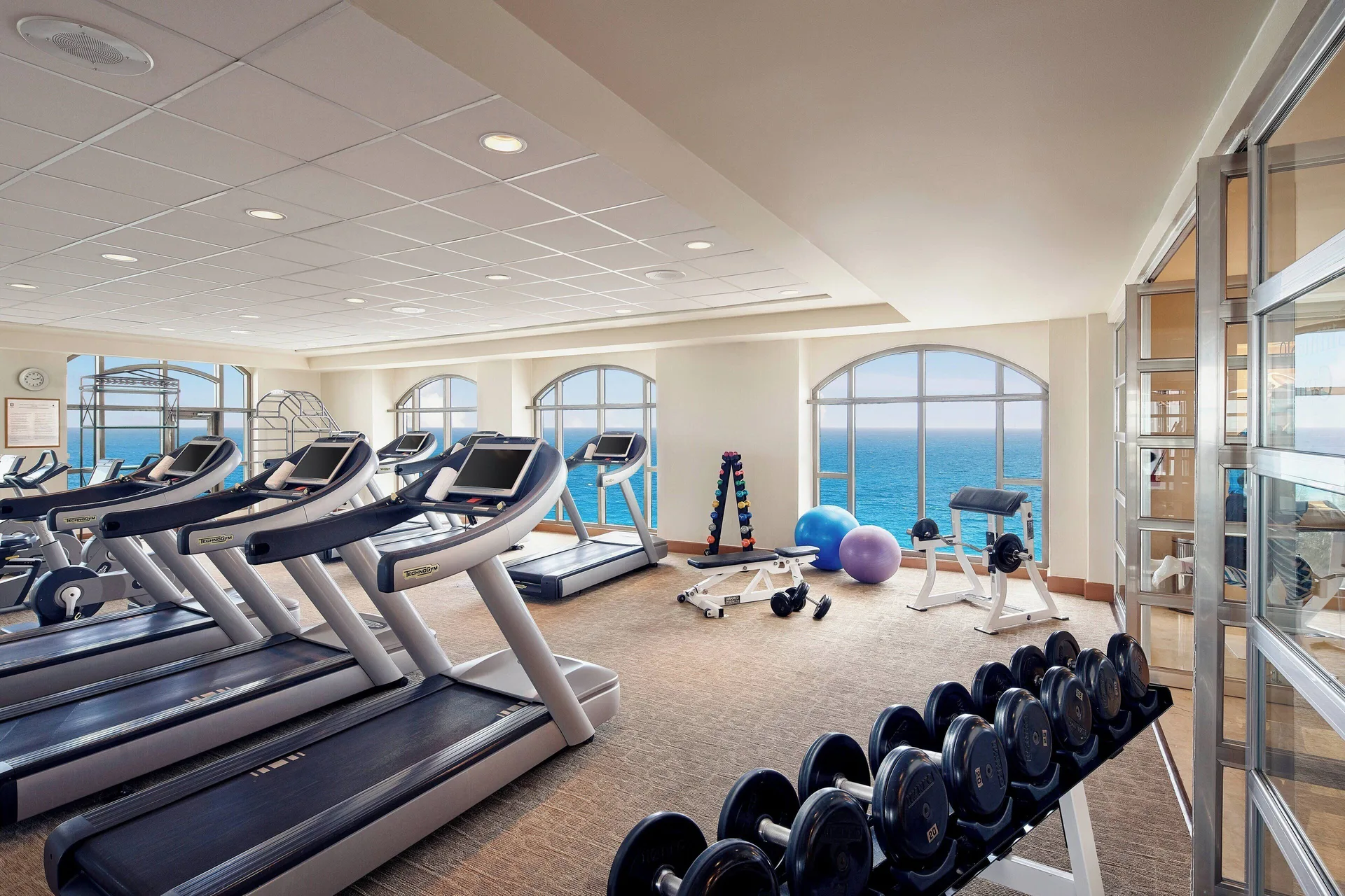 Fitness center with treadmills, weights, and arched ocean-view windows at JW Marriott Cancun Resort & Spa.