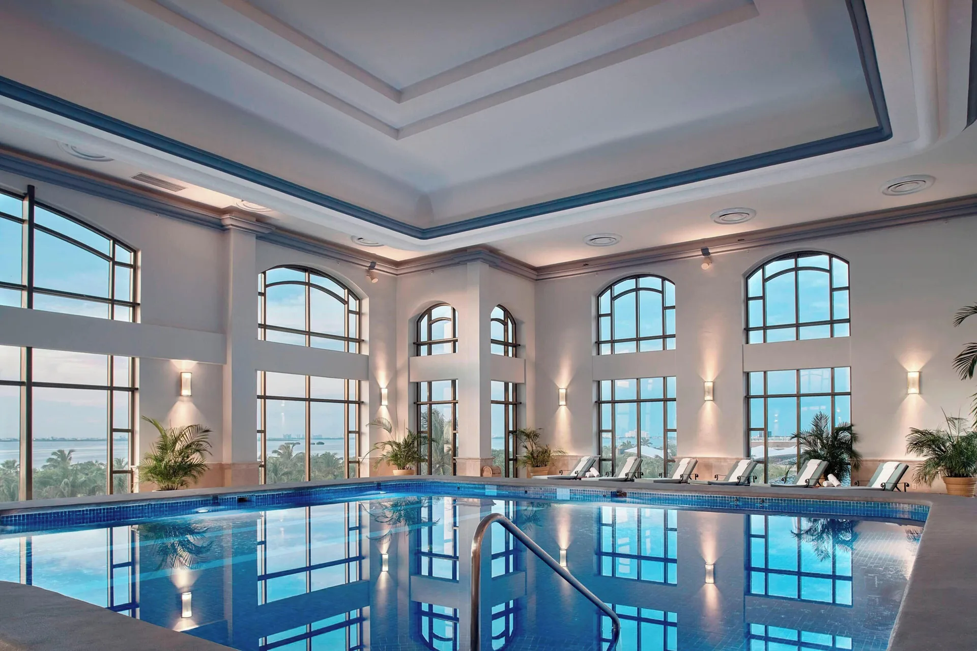 Indoor pool with arched windows and lounge chairs at JW Marriott Cancun Resort & Spa.