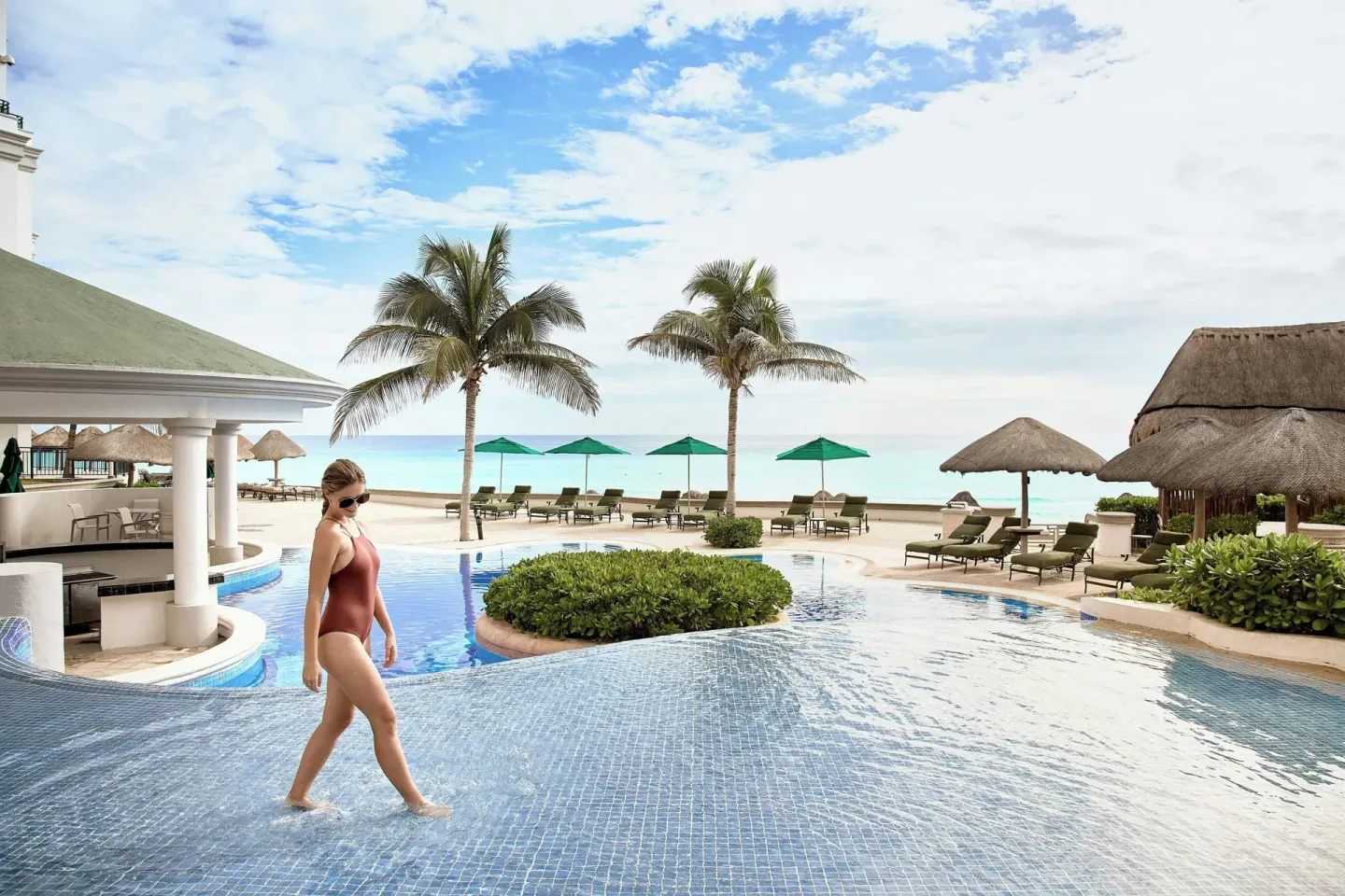 Outdoor pool with palm trees, loungers, and ocean beyond at JW Marriott Cancun Resort & Spa.
