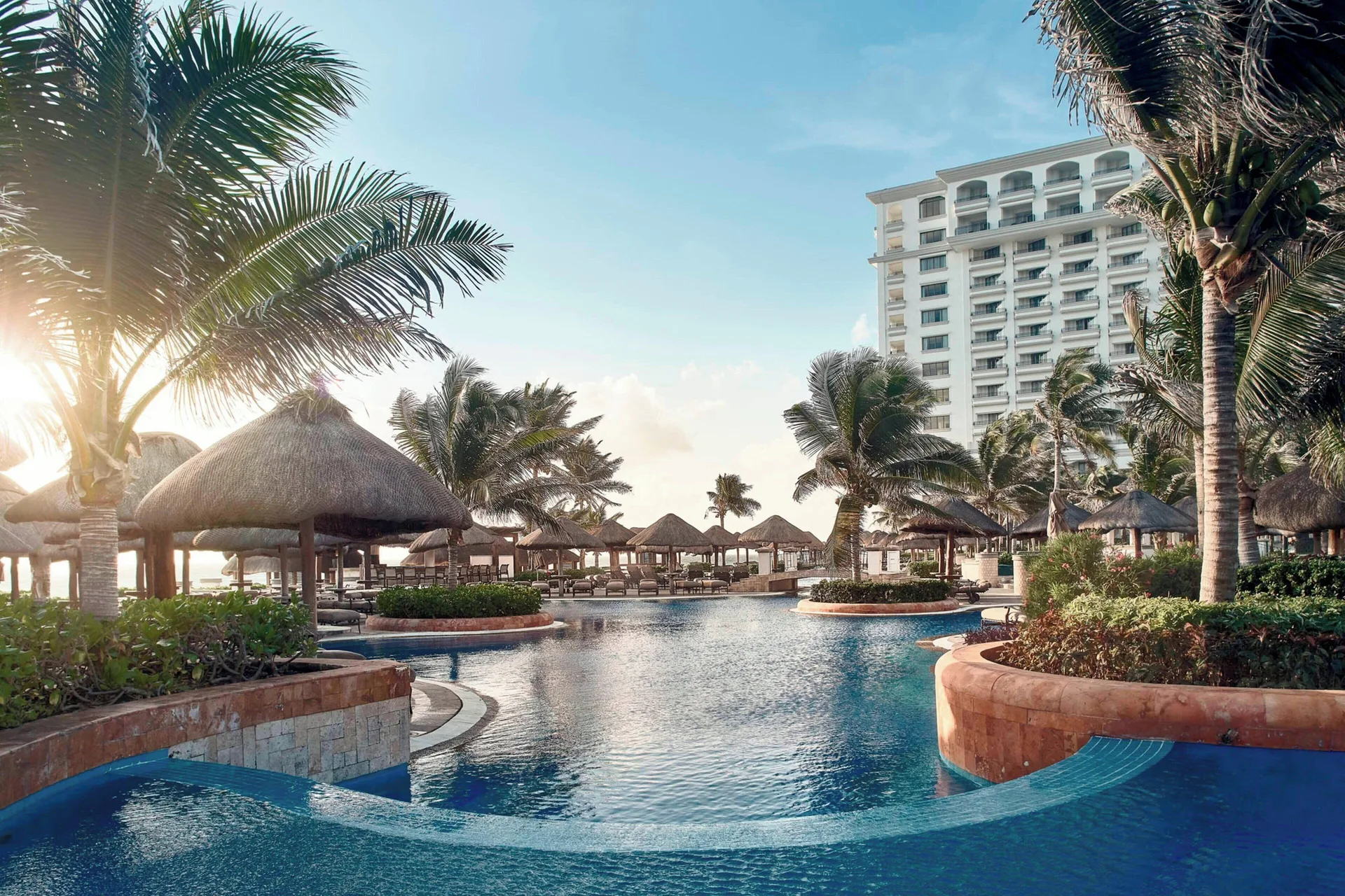 Palm-lined pool with palapas and resort tower at JW Marriott Cancun Resort & Spa.