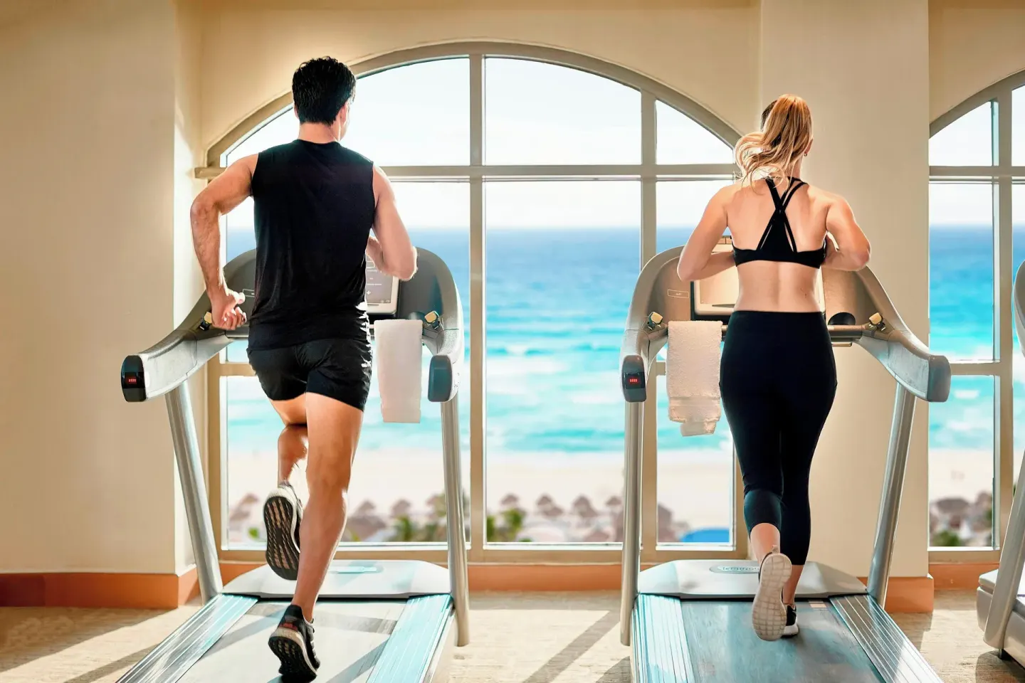 Two guests running on treadmills facing ocean-view windows at JW Marriott Cancun Resort & Spa.