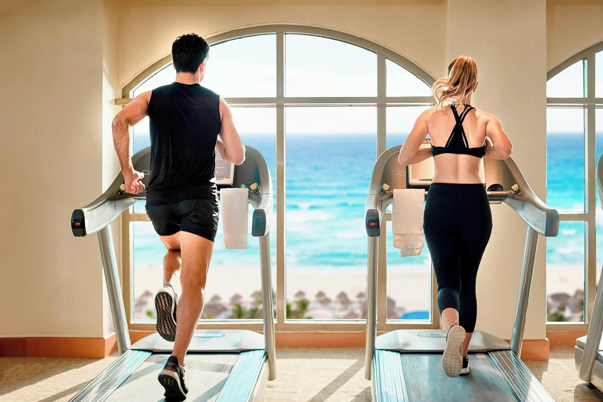 Two guests running on treadmills facing ocean-view windows at JW Marriott Cancun Resort & Spa.