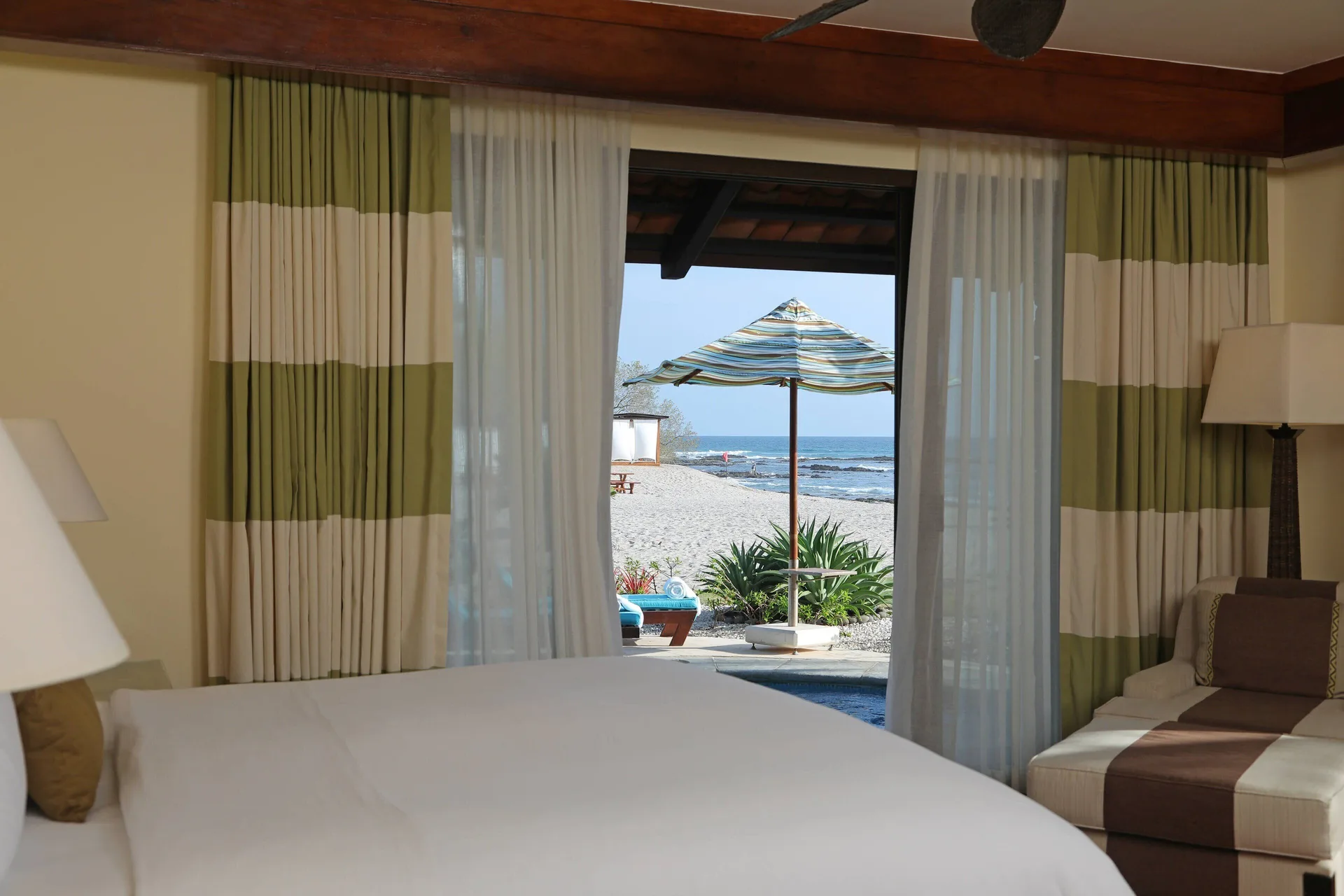 Guest room bed facing a beach patio umbrella at JW Marriott Guanacaste Resort and Spa.