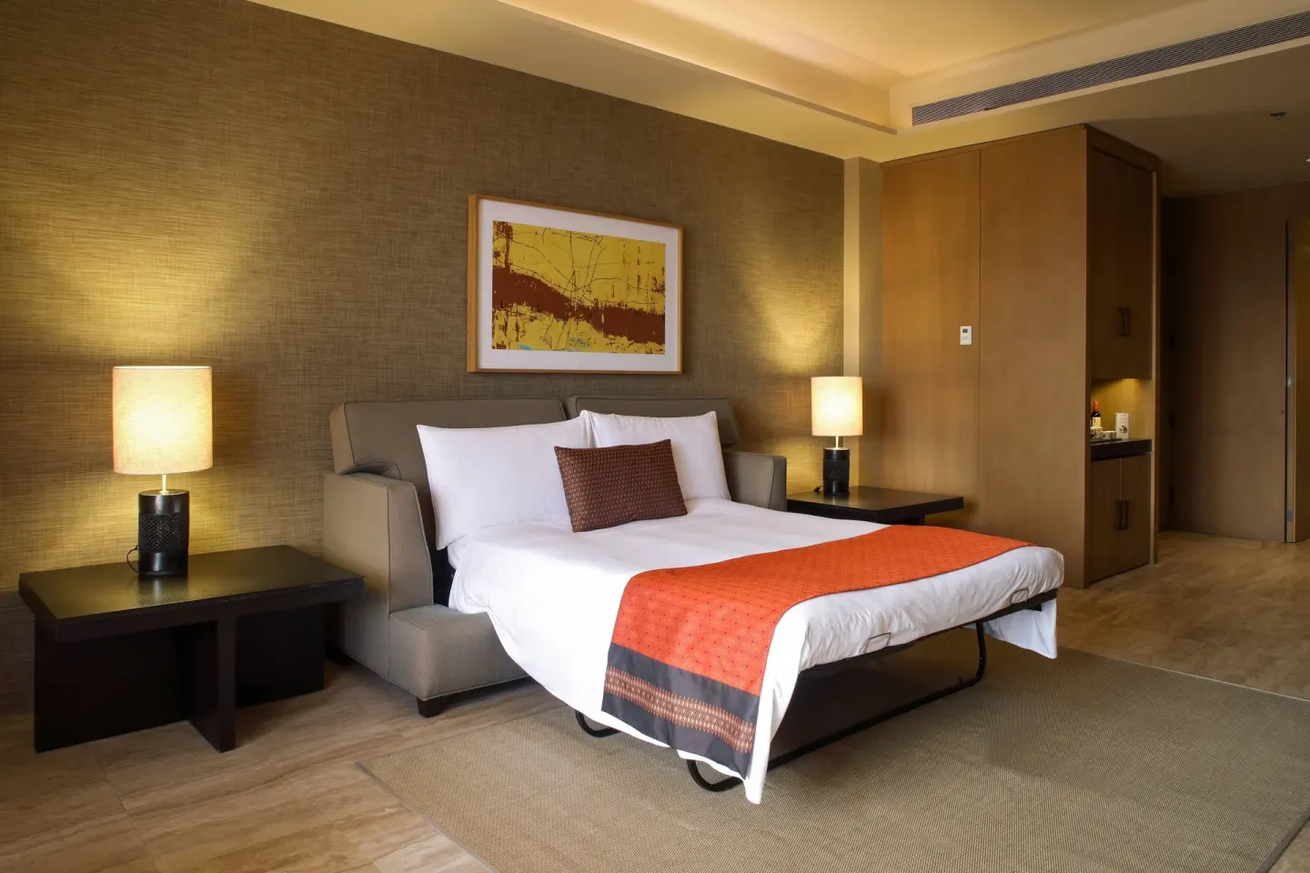 Guest room sofa bed with lamps and wood cabinetry at JW Marriott Los Cabos Beach Resort & Spa.